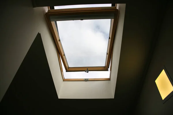 Window in the ceiling. Blue sky with clouds. Attic interior.