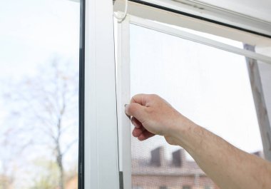 Man is installing the mosquito net on the window. Protection from bugs.
