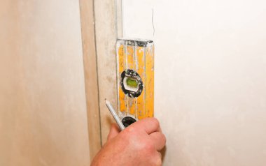 Man is holding a spirit level in hands. Hanging of wallpapers. Maintenance repair works renovation in the flat. Restoration indoors.