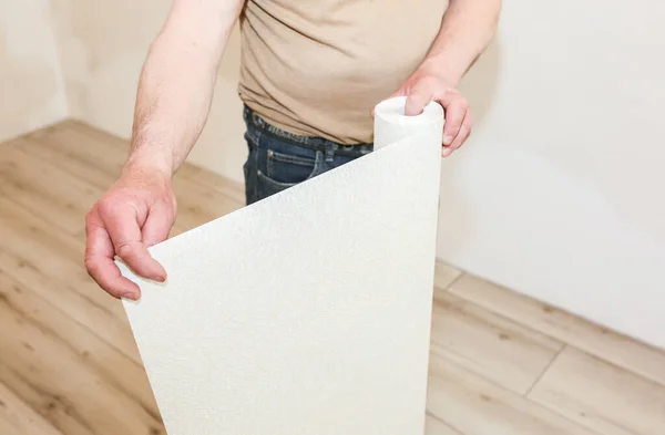 Man is holding roll wallpaper in hands. Maintenance repair works renovation in the flat. Restoration indoors.