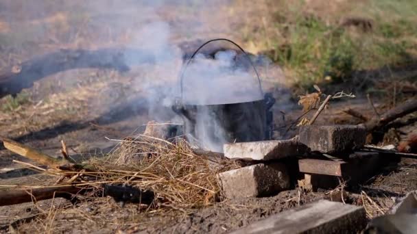 Gătitul mâncării într-o cratiță peste un foc de tabără deschis în fum la apus de soare. Slow motion — Videoclip de stoc