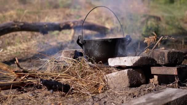 Gătitul mâncării într-o cratiță peste un foc de tabără deschis în fum la apus de soare. Slow motion — Videoclip de stoc