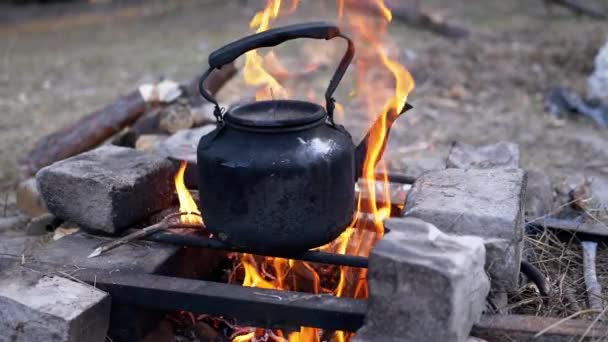 Bătrânul ceainic negru afumat se încălzește peste focul de tabără din pădure. Close up — Videoclip de stoc
