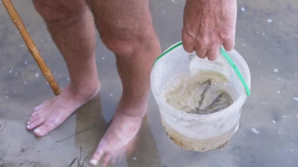 Visser houdt in handen een plastic emmer met een gevangen kleine vis. 4K. Langzame beweging — Stockvideo