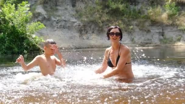 Copilul fericit și mama se scufundă într-un râu puțin adânc, creând valuri, stropi — Videoclip de stoc
