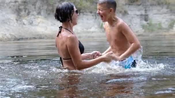 Счастливый ребенок и мама плескаются в мелкой реке, создавая волны, всплески — стоковое видео