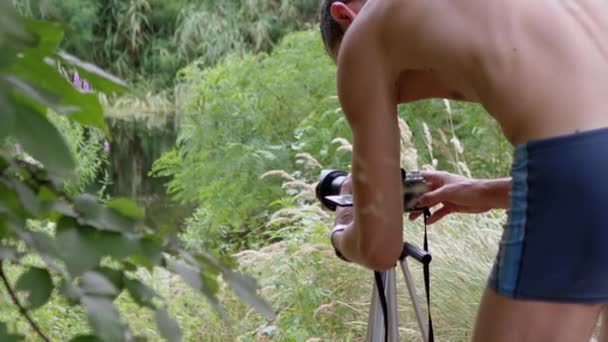 Giovane fotografo, con un corpo nudo, Scattare paesaggi su una riva del fiume. Zoom — Video Stock