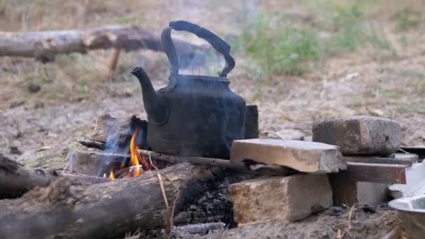 Oude zwarte gerookte ketel verwarmt zichzelf op het rooster van een laaiend, vervagend vreugdevuur. 4K — Stockvideo