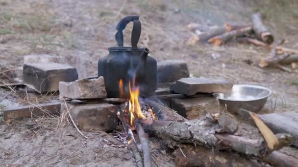 Il vecchio bollitore affumicato nero si riscalda da da solo sulla griglia di un falò ardente e sbiadito. 4K — Video Stock