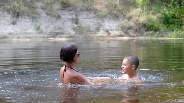 Niño feliz y mamá están salpicando en un río poco profundo, creando olas, salpicaduras — Vídeos de Stock