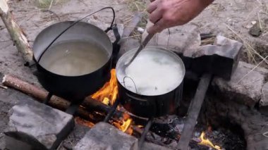 Açık havada, Ormanda Şenlik Ateşi 'nde bir tencerede yemek hazırlayan bir erkek. 4 bin. Kapat.