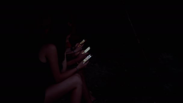 Three Friends in Dark are Looking at Smartphones While Sitting in Wood in Nature — Stock Video