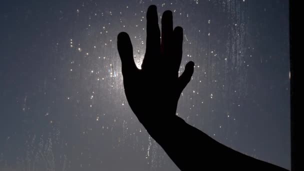 Frau streckt Hand gegen die Sonnenstrahlen aus und berührt ein nasses, dreckiges, vernebeltes Fenster — Stockvideo