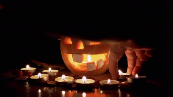 南瓜头背景下的女性手用燃烧的蜡烛装饰餐桌 — 图库视频影像