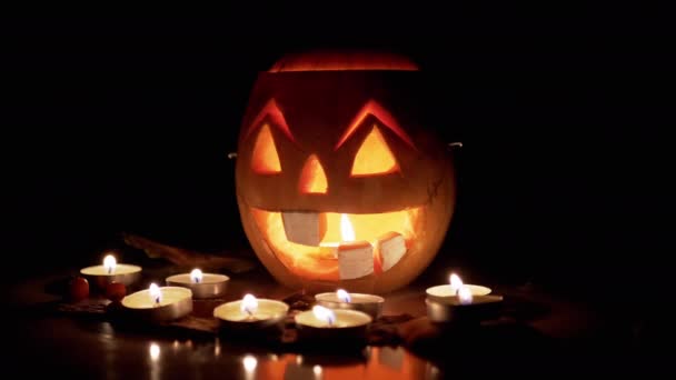 Kürbis mit gruseligem Jack-o-Laternen-Gesicht, brennende Kerzen im dunklen Raum. 4K — Stockvideo