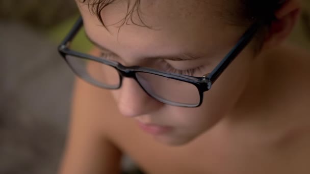 Un niño serio, tranquilo y triste con gafas mira hacia abajo. 4K. De cerca. Movimiento lento — Vídeos de Stock