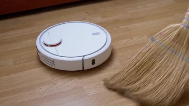 Robot Vacuum Sweeps Debris on Floor na tle zamiatarki. 4K — Wideo stockowe