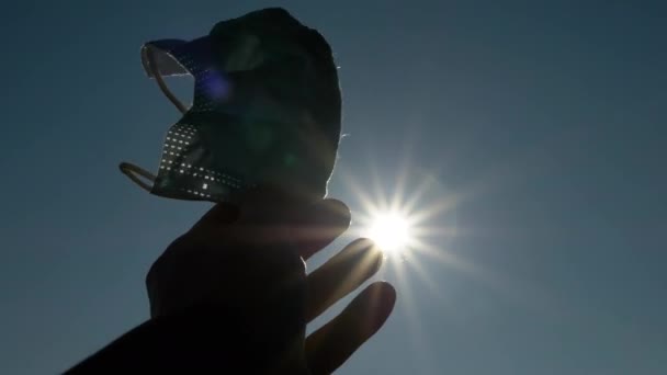 La mano femenina con una máscara en la palma tira a los rayos del sol, el sol. 4K. De cerca. — Vídeos de Stock