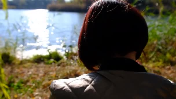 Bezstarostná dívka fotografuje podzimní krajinu, stojící u vody ve slunečních paprscích. 4K — Stock video