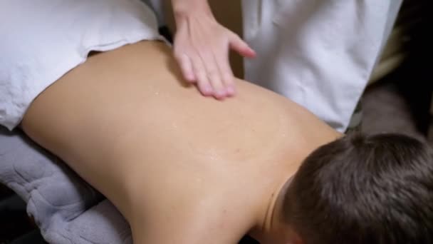 Ręce masażysty masują plecy nastolatka, dziecka w salonie spa. — Wideo stockowe