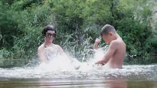 Gelukkig kind en mam zijn spetteren in een ondiepe rivier, het creëren van golven, plons — Stockvideo