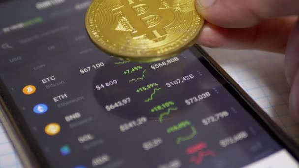 Man roteert Bitcoin Coin Over Smartphone Screen Toont de groei van Cryptocurrency — Stockvideo