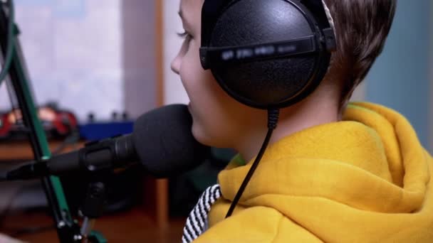 Улыбающийся мальчик-блоггер в наушниках, разговаривая в микрофон приводит видеоблог — стоковое видео