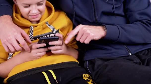 Glücklicher Sohn mit Papa lacht, lehrt neue Apps, schaut aufs Handy, sitzt auf Sofa — Stockvideo