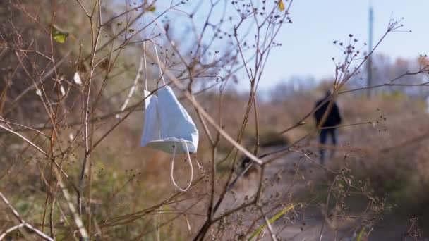 Отброшенная медицинская маска раскачивается на ветру на ветке сухого дерева в лесу. 4K — стоковое видео