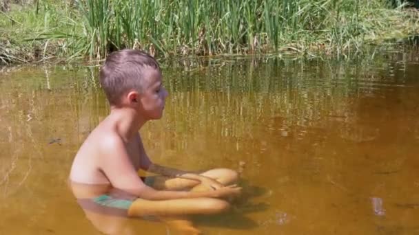 Un niño se sienta en una posición de loto en un río poco profundo, medita al atardecer. 4K — Vídeo de stock