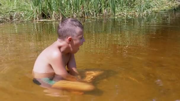 Un niño bostezando dormido se sienta en una posición de loto en un río poco profundo al atardecer. 4K — Vídeo de stock