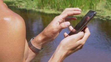 Nehir kıyısında elinde Smartphone olan bir erkek. Kapat.