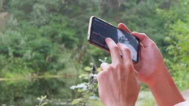 Bir Erkek, Doğa 'daki bir Smartphone' da Kripto Para Biriminin Grafiğini Analiz Eder. 4K