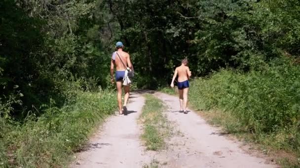 Papá e Hijo están caminando por un sendero arenoso en un bosque verde. Movimiento lento — Vídeo de stock