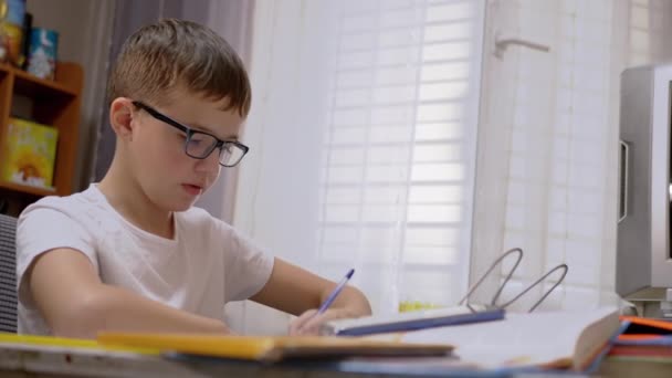 Σοβαρό σχολιαρόπαιδο με γυαλιά γράφει με στυλό στο σημειωματάριο, κάνει μαθήματα. 4K — Αρχείο Βίντεο