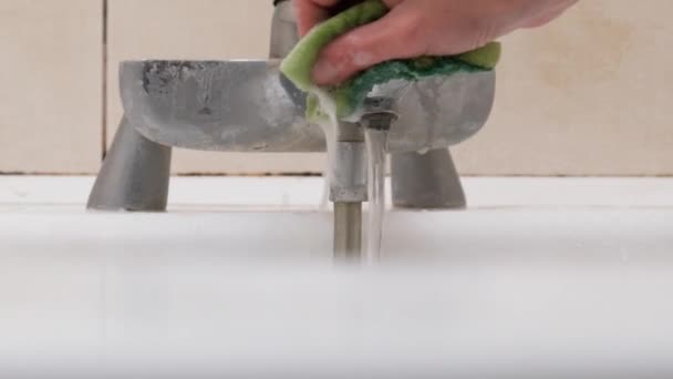 Eine weibliche Hand reinigt einen schmutzigen Wasserhahn mit Schwamm und Waschmittel im Badezimmer — Stockvideo