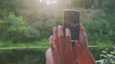 Bir Erkek, Doğa 'daki bir Smartphone' da Kripto Para Biriminin Grafiğini Analiz Eder. 4K