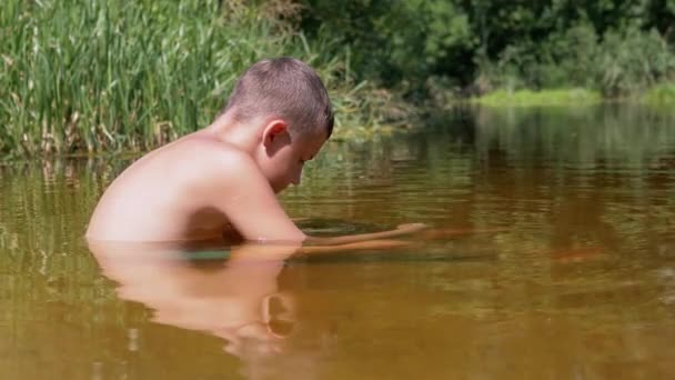 Side View of a Child Sitting Waist-Deep in Water in Shallow River at Sunset. 4K — Stock Video