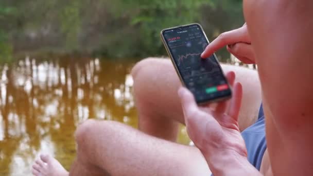 Man Slappna av på stranden Ser ut som en Cryptocurrency Candlestick diagram i en mobil app — Stockvideo