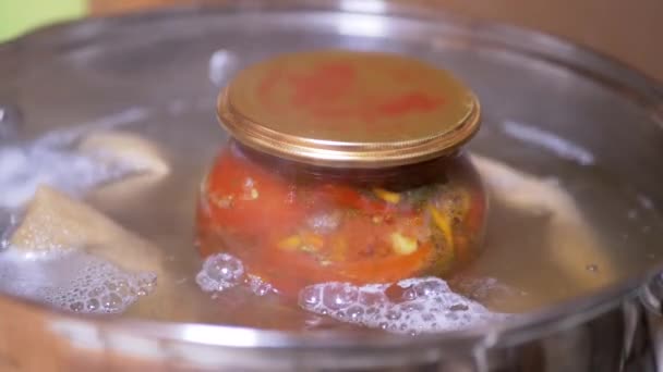 Proceso de esterilización de un frasco de tomates en escabeche en una cacerola de agua hirviendo — Vídeo de stock
