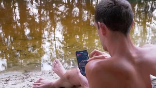 Masculino Relaxante na praia parece um gráfico de castiçal criptomoeda em um aplicativo móvel — Vídeo de Stock