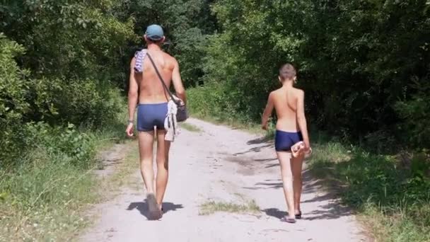 Pai e filho estão caminhando ao longo de um caminho arenoso em uma floresta verde. Movimento lento — Vídeo de Stock