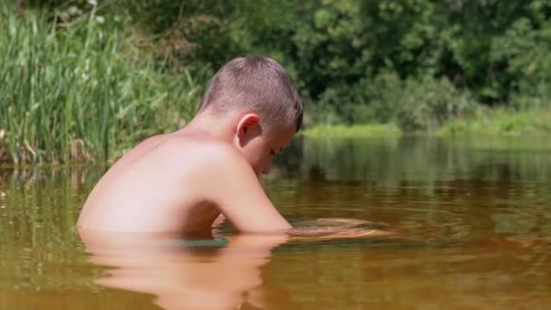 Side View of a Child Sitting Waist-Deep in Water in Shallow River at Sunset. 4K — Stock Video