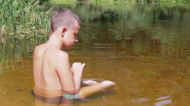 Дитина сідає в лотосове положення в мілководді на Сансет. 4К. Зачиніть. — стокове відео