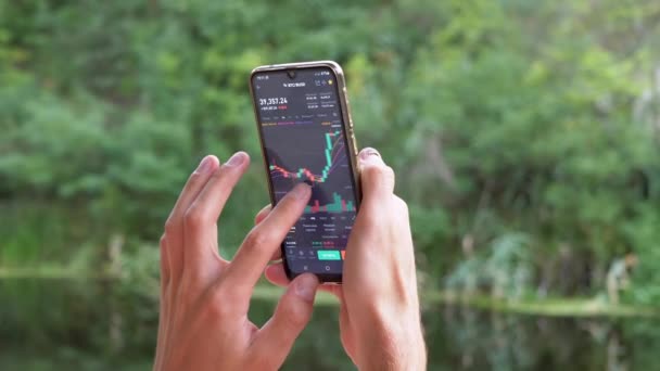 Bir Erkek, Doğa 'daki bir Smartphone' da Kripto Para Biriminin Grafiğini Analiz Eder. Büyüt — Stok video
