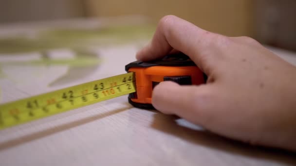 Vrouwelijke Hand drukt op de knop van een Orange Tape Measure met een Return Spring — Stockvideo