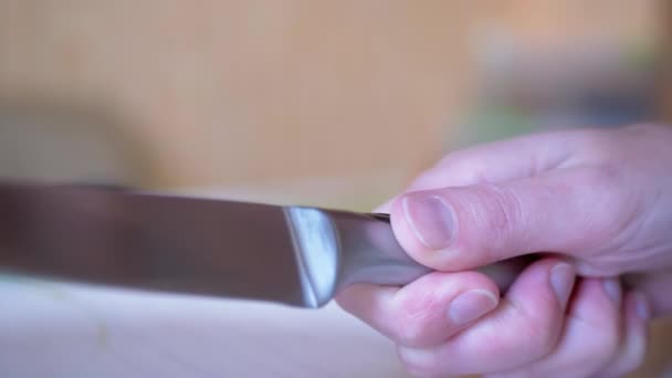 Una mano de mujer sostiene un cuchillo de cocina largo y afilado sobre la superficie de la mesa. 4K — Vídeo de stock