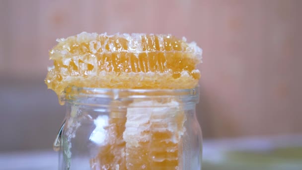 Gotas de flujos de miel esparcen una capa gruesa en un tarro de vidrio en un panal de abeja. 4K — Vídeos de Stock