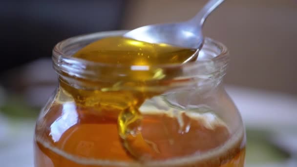 Een vrouwelijke hand pikt op met een transparante, vloeibare honing uit een glazen pot — Stockvideo