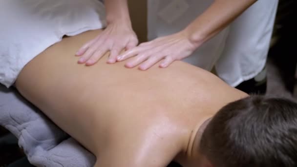 Mãos do massagista estão massageando nas costas de um adolescente, uma criança em um salão de Spa — Vídeo de Stock